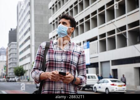 Kaukasischer Mann, der eine kovidte 19-Coronavirus-Maske außerhalb und mit seinem Telefon trägt Stockfoto