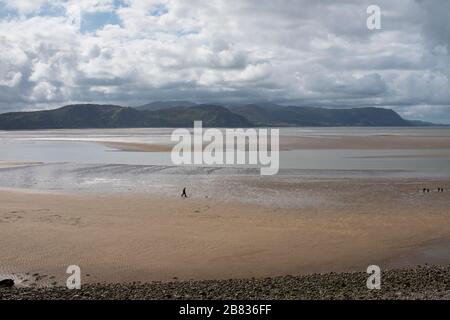 Ein Mann, der am North Shore Strand, Llandudno, mit Snowdonia im Hintergrund läuft. Stockfoto