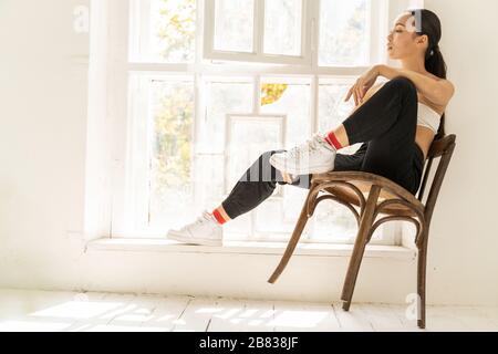 Junge Frau, die in der Nähe des Fensters im Zimmer sitzt Stockfoto