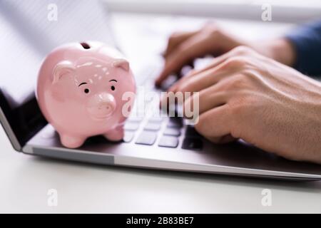 Nahaufnahme der Geschäftsmann Hand Arbeiten am Laptop mit rosa Sparschwein Stockfoto