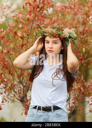 Schönes nachdenkliches Teenager-Mädchen im Herbstkranz aus Blättern und Beeren auf dem Hintergrund roter Blätter Stockfoto