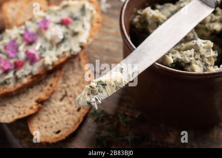 Kräuterbutter aus jungen Brennnesseln auf einem Messer, mit Brot im Hintergrund Stockfoto