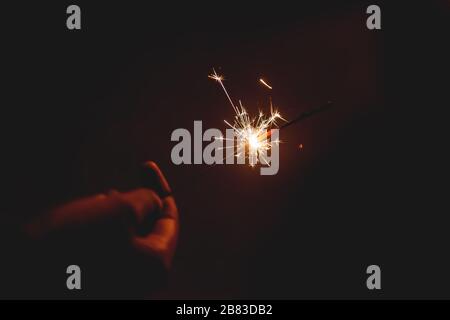 Brennender Funkenstift Sternenfeuerwerk Pyrotechnik Dunkelschwarz warmer Hintergrund an der Hand gehalten Stockfoto