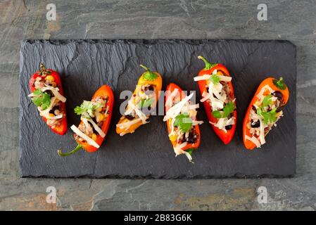 Gefüllte Mini-Paprika mit Wildreis, Käse, Bohnen, Mais und Cilantro. Über der Ansicht auf dunklem Schieferhintergrund. Stockfoto