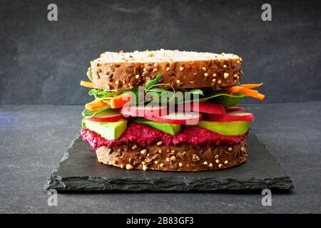 Superfood Sandwich mit Zuckerrüben Hummus, Avocado, Gemüse und Grüns, auf Vollkornbrot gegen einen Schiefer Hintergrund Stockfoto