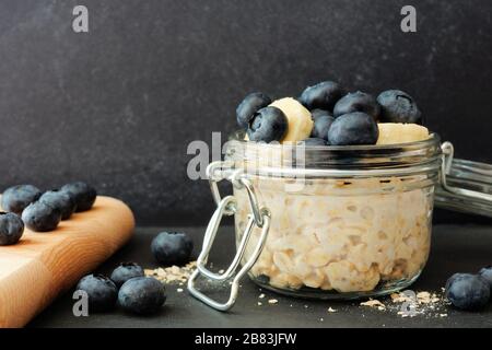 Übernachtung Hafer mit frischen Blaubeeren und Bananen in einem Krug vor dunklem Hintergrund Stockfoto