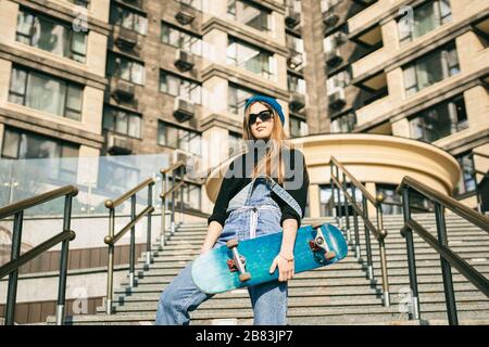 Urbane Frau mit Skate. Hipper-Mädchen mit Skateboard in der Stadt. Konzept für Extremsport und Emotionen. Alternativer Lebensstil. Modische Hüftmädchenhaltung Stockfoto