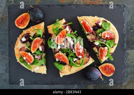 Herbst Fladenbrot Pizza mit Feigen, Rucola und Ziegenkäse, Overhead Szene auf schiefer Hintergrund Stockfoto