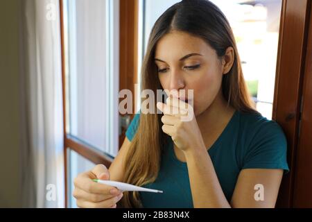 COVID-19 Pandemie Coronavirus Trockenhusten Halsfieber Sorgen Frau Temperaturkontrolle mit Thermometer zu Hause Symptom von SARS-COV-2. Mädchen prüfen Stockfoto