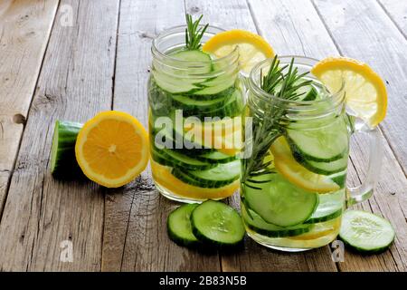 Zwei Gläser aus Maurerglas mit Zitronenwasser, Gurke und Rosmarin auf rustikalem Holzhintergrund Stockfoto