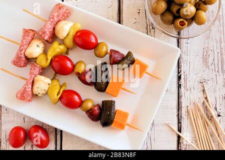 Spieß-Häppchen mit Käse, Fleisch und Pickeln Blick über den Kopf auf einen weißen Holzhintergrund Stockfoto