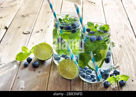 Zwei Maurer-Glas-Brille aus Blaubeere, Kalk, Minzentox-Wasser mit Strohhalmen vor einem rustikalen Holzhintergrund Stockfoto