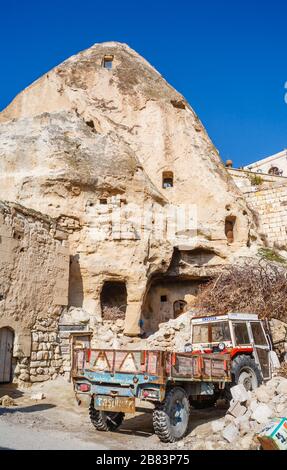 Rot-blau lackierter Anhänger und Traktor, der im historischen Gebiet von Göreme neben einer stillgehaltenen Felswohnung aus Troglodyten, Kappadokien, Türkei, geparkt ist Stockfoto