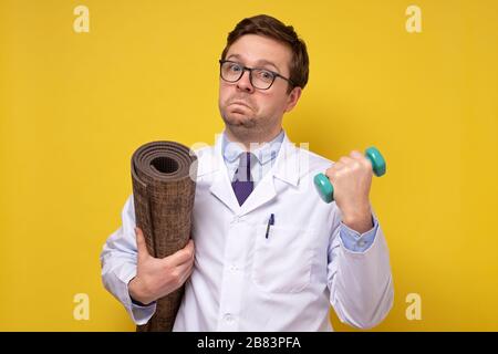 Ein reifer kaukasischer Mannarzt, der Hanteln hält und Ratschläge zu einem gesunden Lebensstil gibt. Sport- und Medizinkonzept. Stockfoto