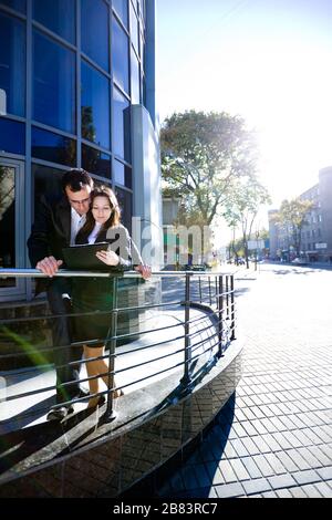 Mann unterschreibt Papiere in Händen einer Frau, während er bei sonnigem Wetter vor dem Bürogebäude auf der Straße steht Stockfoto