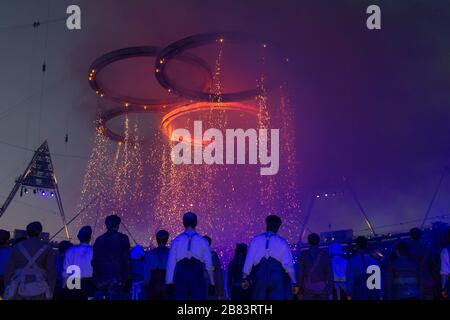 Darsteller im Londoner Stratford Olympic Stadium 2012 beim betrachten der Olympics-Ringe, die während der Eröffnungsfeier Feuerfunken sprühen, kleiden sich um Stockfoto