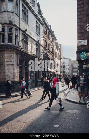 London, Großbritannien - 06. März 2020: Menschen, die auf der Wardour Street in Soho, einem Gebiet von London, das für LGBTQ+ Bars, Restaurants und Clubs berühmt ist, bei Sonnenuntergang spazieren gehen. Stockfoto