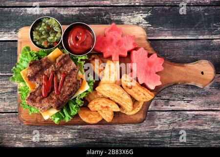 Tages-Picknick-Szene in Kanada mit Hamburgern in Ahorn-Blattform und Wassermelone auf einem Paddelbrett über rustikalem Holz Stockfoto