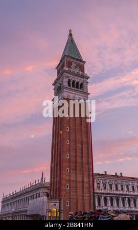 Vertikaler Schuss des Campanile (Glockenturm) über dem Markusplatz, Venedig. Cirrus Wolken - pink angezündet durch Sonneneinstrahlung - verbergen teilweise einen Vollmond. Stockfoto