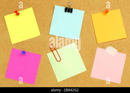 Leere Haftnotizen verschiedener Farben und Befestigungselemente auf einem Bulletin Board Stockfoto