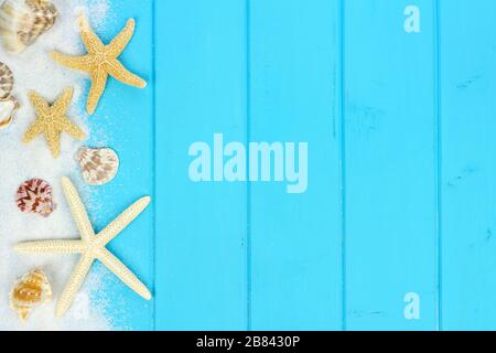 Sommerliche Seitengrenze von Sand, Meeresschalen und Sternenfischen auf blauem Holzgrund Stockfoto