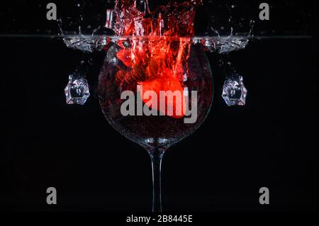 Erdbeere spritzt in Glas Wein, das in Wasser auf schwarzem Grund eingetaucht ist Stockfoto