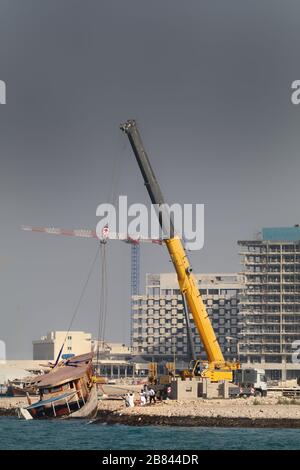 Ein Kran mit einem sinkenden Holzboot in Doha, Katar Stockfoto