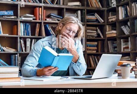 Langweiliger müde Kerlstudent gähnende Lesebuch Studium in Bibliothek. Stockfoto