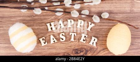 Aufschrift Happy Easter, Weidenzweige und bunte Eier umhüllte Wollsaite auf rustikaler Tafel, festliches Dekorationskonzept Stockfoto