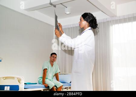 Ein männlicher Patient saß auf dem Bett. Unter Behandlung und unter Aufsicht eines Arztes, in dem der Arzt die Ergebnisse des Röntgenfilms untersucht. Stockfoto