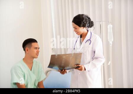 Ein männlicher Patient saß auf dem Bett. Unter Behandlung und unter Aufsicht eines Arztes, in dem der Arzt die Ergebnisse des Röntgenfilms untersucht. Stockfoto