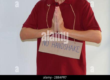 Closeup Pappschild mit Handschrift KEIN HANDSCHLAG, der am Hals eines Mannes hängt, der namaste ausführt, die neue Art der Begrüßung durch Coronavirus outbr Stockfoto