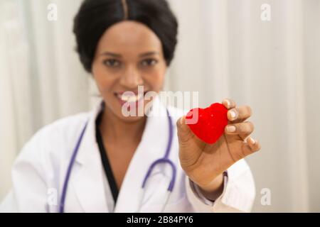 Afrikanischer weiblicher Arzt mit Stethoskopstativ und einem roten Herzsymbol. Stockfoto