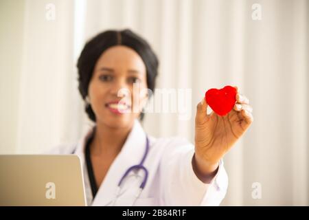 Afrikanischer weiblicher Arzt mit Stethoskopstativ und einem roten Herzsymbol. Stockfoto