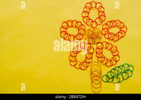 Bunte Gummibänder in Blumenform auf gelbem Hintergrund mit leerem Raum für Hintergrund und abstraktes Konzept. Stockfoto
