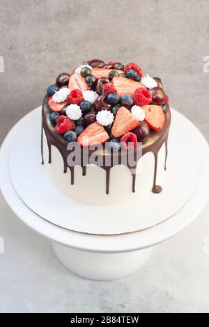 Weißer Kuchen mit geschmolzener dunkler Schokolade, frischen Erdbeeren, Blaubeeren, Himbeeren und Kirschen auf grauem Grund Stockfoto