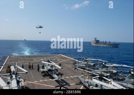 SOUTH CHINA SEA (17. März 2020) - Segler, die dem amphibischen Transport-Dockschiff der San Antonio Klasse USS Green Bay (LPD 20) zugeordnet sind, stehen für Fracht da ein SH-60R-Hubschrauber, der dem amphibischen Angriffsschiff USS America (LHA 6) zugeordnet ist, ihn während eines vertikalen Nachschubs auf das Flugdeck liefert. Green Bay, Teil des America Expeditionary Strike Group 31. Marine Expeditionary Unit Teams, ist im 7. US-Flottengebiet tätig, um die Interoperabilität mit Verbündeten und Partnern zu verbessern und als einsatzbereite Einsatzkräfte zur Verteidigung von Frieden und Stabilität in der Region Indopazifik zu dienen. (USA Marine p Stockfoto