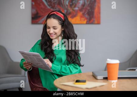 Junge Frau, die in einem Büro sitzt und eine Zeitung in der Hand hat. Stockfoto