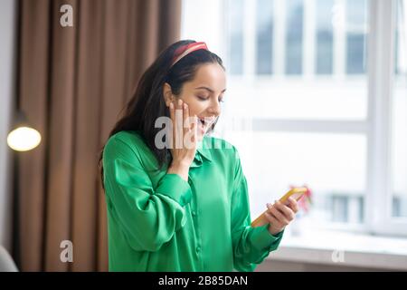 Frau in einer smaragdgrünen Bluse mit Blick auf Smartphone in der Hand. Stockfoto