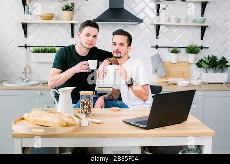 Zwei glückliche schwule Männer im Homewear verbringen den Morgen in der Küche. Fröhliche schwule Männer frühstücken morgens zu Hause. Stockfoto