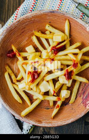 Pommes frites auf schwarzer Oberfläche anprittieren. Kanadisches Gericht mit Kartoffeln, Käse und Sauce Stockfoto