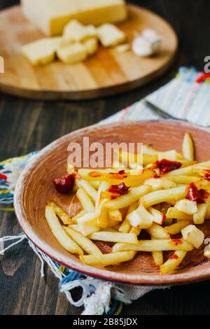 Pommes frites auf schwarzer Oberfläche anprittieren. Kanadisches Gericht mit Kartoffeln, Käse und Sauce Stockfoto