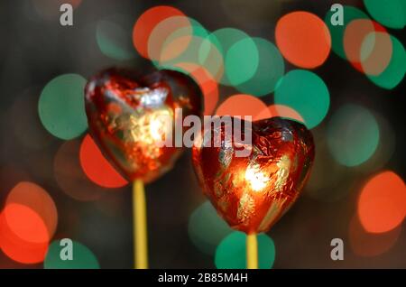 Schokoladenkäuze zum valentinstag. Schokolade in roter Herzform auf Lolly Stick. Schokoladenherz in roter Folie auf einem Stock auf einem bokeh verschwommenen Hintergrund Stockfoto