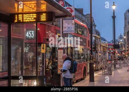 Langsamer Stadtverkehr. London Buses in Whitehall, Central London, UK am frühen Abend. Männlicher Bussgast wartet an der Bushaltestelle. Öffentliche Verkehrsmittel. Stockfoto