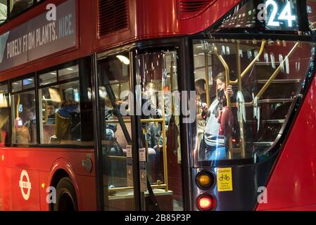 Nahaufnahme der Busgäste (durch Hintertüren, Fenster gesehen), die nachts im roten Doppeldecker-London-Bus sitzen. Öffentliche Verkehrsmittel in London. Stockfoto