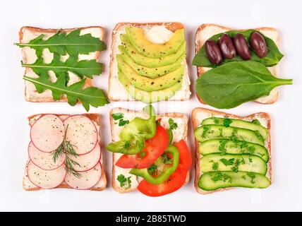 Set mit Toastbrot und verschiedenen veganen Belägen auf weißem Hintergrund, Draufsicht. Toasts mit Avocado, Spinat, Arugula und anderen Gemüsearten Stockfoto