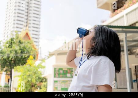 Mädchen, die weiße Hemden tragen, verwenden ein blaues Fernglas. Hintergrund ist ein hohes Gebäude. Stockfoto