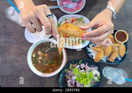 Thailändische Küche ist bei Menschen auf der ganzen Welt sehr beliebt. Die Hände von Frauen, die gebratene Hühnerflügel, thailändische Küche fangen und sie essen. Der Rücken Stockfoto