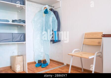 Schutzanzug mit Handschuhen, Maske und Brille in garderobe mit Anderskleidung bei Überregung und Panicing Person zu Hause Stockfoto