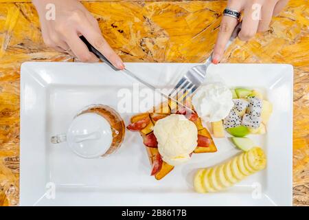 Die Hand der Frau, die ein Messer und eine Gabel hält, um Honey Santos von der Kälte zu essen, die sie mag. Eis, das auf Brot gelegt wird und Bana enthält Stockfoto